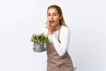 Young blonde gardener woman girl holding a plant over isolated white background whispering something