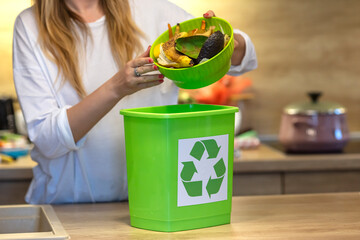 Woman recycling organic kitchen waste by composting in green container during preparation of meal. A young girl throws vegetable cuttings in a compost bucket. Plastic compost bucket.