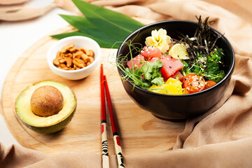 Poke salad with tuna in a bowl. Ingredients fresh tuna, cherry tomatoes, marinated seaweed, rice, takuan, Ponzu sauce, Teriyaki sauce, nori, sesame seeds, lime, cilantro. Asian seafood salad concept.