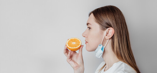 Loss of smell long banner. Caucasian young woman in a medical mask sniffing an orange on a white...