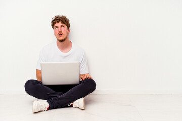 Young caucasian man sitting on the floor holding on laptop isolated on white background tired of a repetitive task.