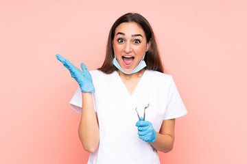 Woman dentist holding tools isolated on pink background with surprise facial expression
