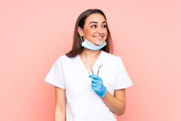 Woman dentist holding tools isolated on pink background laughing and looking up