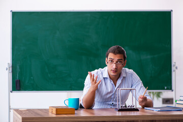 Young male teacher physicist in front of blackboard
