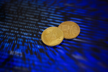 Two gold bitcoin coins on the background of lines of program code