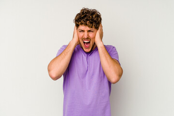 Young caucasian man isolated on white background covering ears with hands trying not to hear too loud sound.