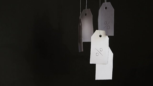 White tags with the percent sign hang on strings on a black background with shadows. Commerce, discount, sale, trade offer. Copy space, mock up. Black Friday