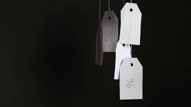 White tags with the percent sign hang on strings on a black background with shadows. Commerce, discount, sale, trade offer. Copy space, mock up. Black Friday