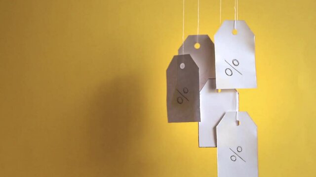 White tags with the percent sign hang, flying and swaying on strings on a yellow background with shadows. Commerce, discount, sale, trade offer. Copy space, mock up.