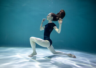 Fototapeta na wymiar beautiful girl in a black leotard doing gymnastic exercises underwater on a blue background 