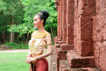 Asian woman in luxury traditional Thailand costume dress soft elegant standing in ancient Cambodia temple on outdoor morning. Invitation advertisement to travel beautiful Thai culture with copy space