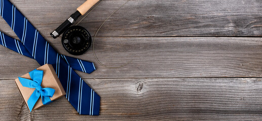 Fathers day concept with blue dress tie, fly fishing reel and a giftbox on rustic wooden background