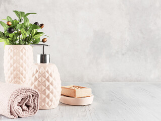 Bathroom decor composition. Soap dispenser, towel, natural soap and vase with olive tree on a gray background. Space for text.