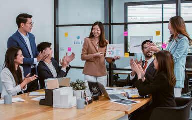 Asian beautiful business woman wearing formal suit, discussing and presenting financial graph or chart to her mixed race colleagues in meeting room at indoor office or workplace.