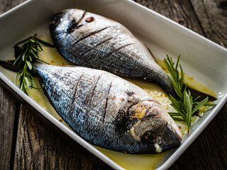 Fresh dorada and herbs in cooking pot on wooden background
