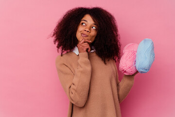 Young african american woman holding a sewing threads isolated on pink background looking sideways with doubtful and skeptical expression.