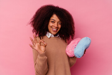 Young african american woman holding a sewing threads isolated on pink background cheerful and confident showing ok gesture.