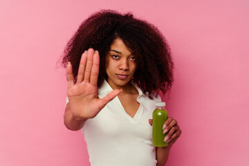 Young african american woman drinking a healthy smoothie isolated on pink background standing with outstretched hand showing stop sign, preventing you.