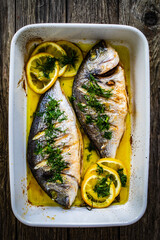 Roast dorada with lemon and rosemary in cooking pan on wooden table

