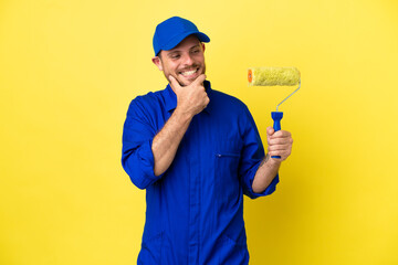 Painter Brazilian man isolated on yellow background looking to the side and smiling