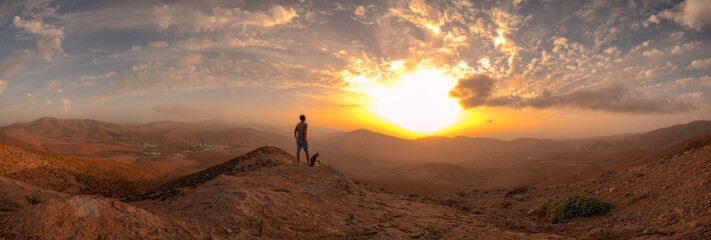 Atardecer en la montaña con persona y perro mirando el sol