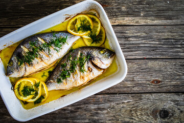 Roast dorada with lemon and rosemary in cooking pan on wooden table

