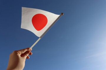 A hand holding a Japanese flag. National flag of Japan in the blue sky. Stock photo template with copyspace