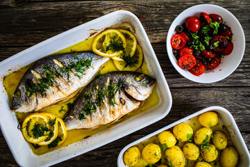 Roast dorada with lemon ,rosemary and potatoes in cooking pan on wooden table
