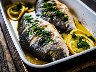 Roast dorada with lemon and rosemary in cooking pan on wooden table

