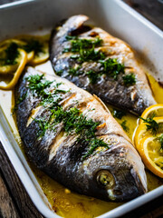 Roast dorada with lemon and rosemary in cooking pan on wooden table
