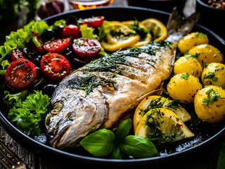 Roast dorada with potatoes and vegetables on wooden table
