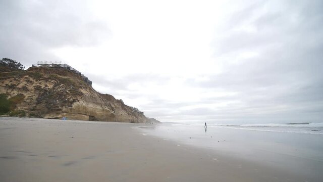 Silhouette of Distant Person Walking on Sandy Beach Under Cliff and Cloudy Sky. Solana Beach, San Diego County, California USA