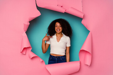 Young African American woman in torn paper isolated on blue background person pointing by hand to a shirt copy space, proud and confident