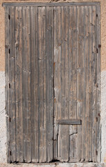Background of an old weathered closed wooden door that is in portrait format in an old wall.
