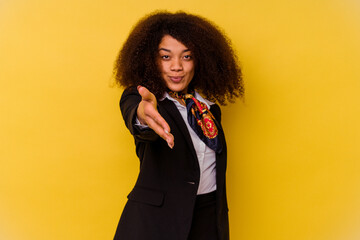 Young African American air hostess isolated on yellow background stretching hand at camera in greeting gesture.