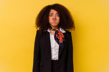 Young African American air hostess isolated on yellow background blows cheeks, has tired...