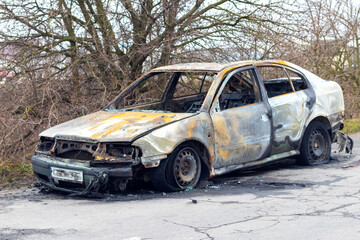 Obraz na płótnie Canvas Burned car after an accident on the asphalt road. Side view. Arson of a car, criminal showdowns