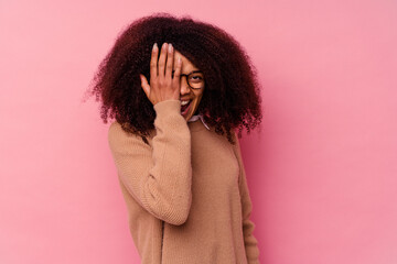 Young african american woman isolated on pink background having fun covering half of face with palm.