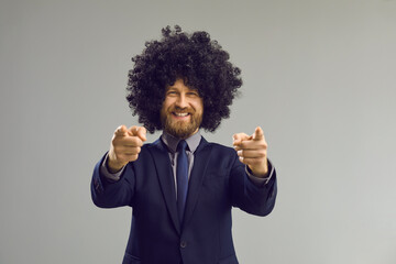 Portrait of funny happy smiling bearded man in formal suit and crazy curly wig pointing double...