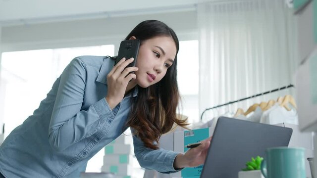 Asian entreprenuer woman online seller confirming orders from customer on the phone. Online web store owner taking order on phone, texting message online. Phone call receive from customer