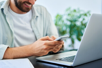 Closeup of happy man texting on mobile phone smartphone while using laptop