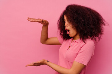 Young african american woman isolated on pink background shocked and amazed holding a copy space between hands.