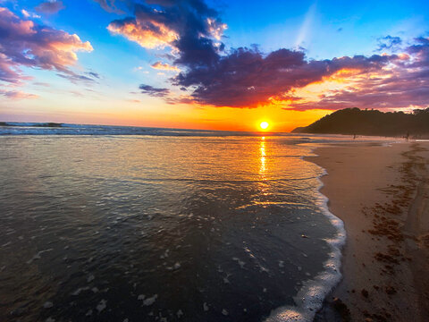 Atardecer espectacular con cielo naranja y p&uacute;rpura reflejado en el mar sobre playa de arena en Jac&oacute;, Costa Rica