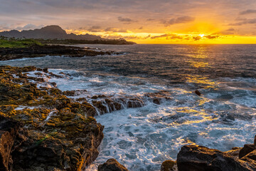 Sunrise on southern Kauai shoreline as waves splash on the rocky shore, Haupu Mountain in the background, Poipu, Koloa, Kauai