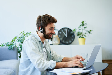 Home office concept. Young man with headset working remotely using laptop