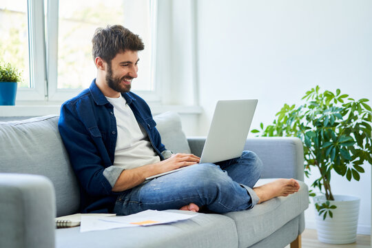 Young Man Study At Home Sitting On Sofa Using Laptop