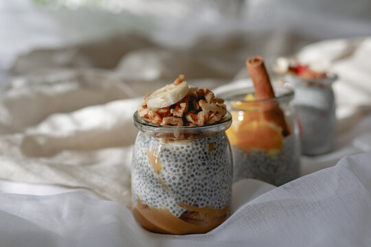 Strawberry, Banana, Orange, Chia Pudding In glass jar on a wooden plate on White bed in Sunlight through the window