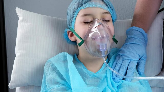little patient in shirt, child, boy lies, facial oxygen mask, concept of medical care, anesthesiology and intensive care, oxygen therapy, treatment of coronavirus, COVID-19