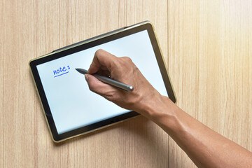 hand writing note on tablet and with pens on wood table, new style of technology to note and take a...