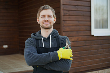 Portrait of young man gardener in gloves and black apron holding pruner